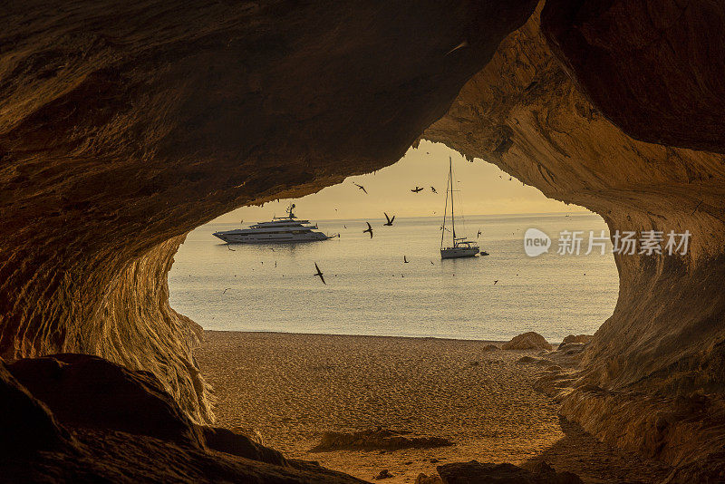 意大利撒丁岛，Cala Luna岩洞，夕阳西下，背景是帆船。